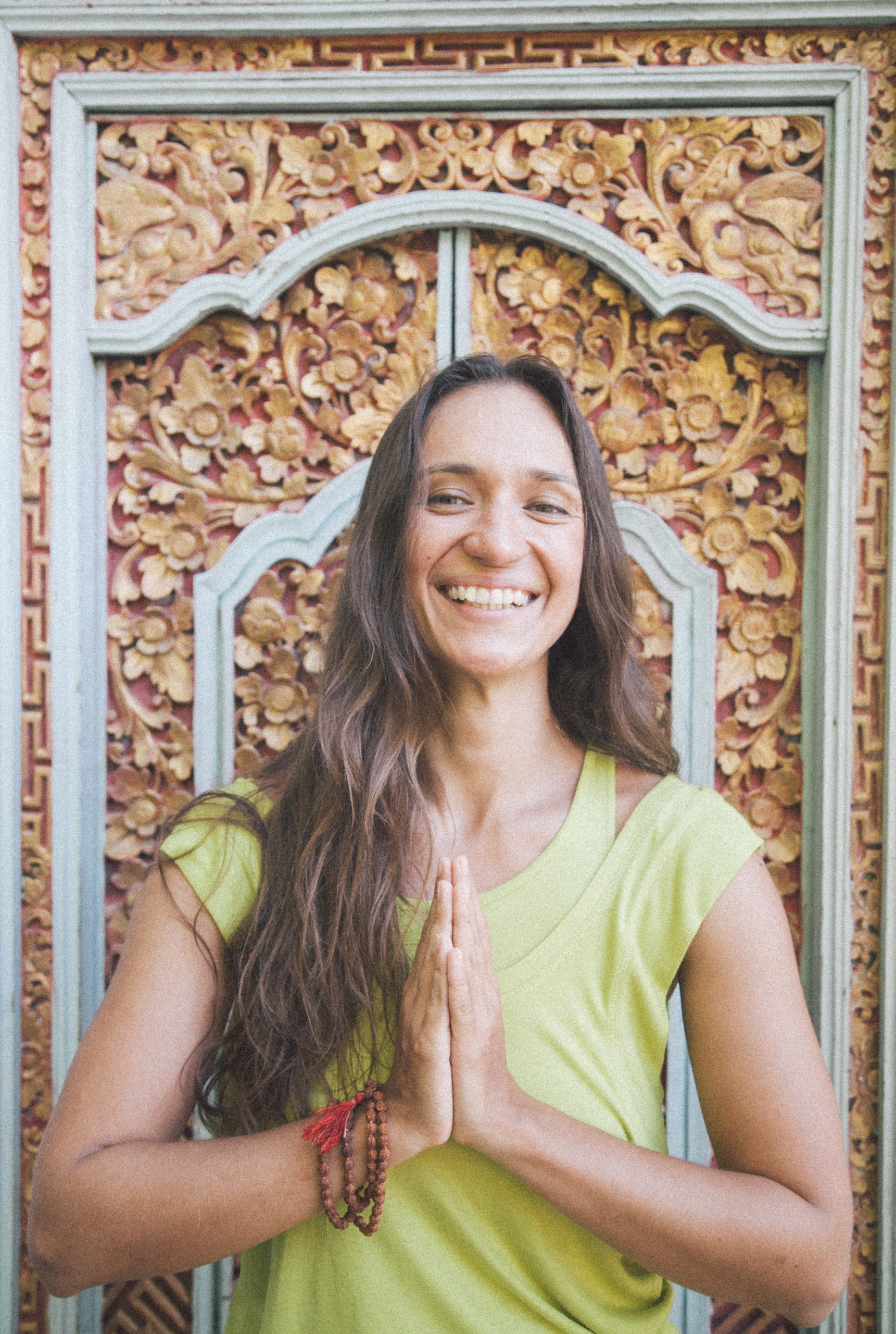 Alena smiling with her palms joined in front of a carved Balinese door